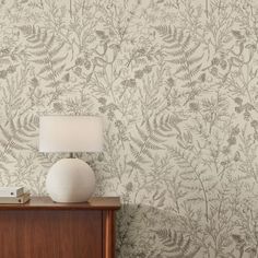 a white lamp sitting on top of a wooden dresser next to a wallpapered wall