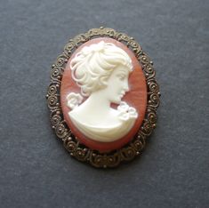 Vintage cameo brooch. Moulded plastic cameo, orange with white figure. Ornate / filigree type metal back, signed Western Germany. Pin and safety clasp. Good condition front - the metal at the back has some tarnish. 5cm x 4cm. Victorian Style White Cameo Brooches, Vintage Orange Metal Jewelry, Victorian Style White Cameo Brooch, Antique Cameo Brooch Collectible, Vintage White Cameo Brooches, White Oval Cameo Brooches, Vintage White Cameo Brooch, Antique White Cameo Brooch, Classic Cameo Collectible Brooches