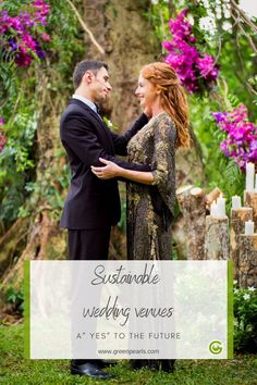 a man and woman standing next to each other in front of trees with purple flowers