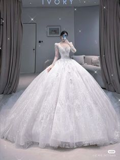 a woman in a white wedding dress standing next to a window with curtains on it