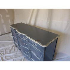 an old blue dresser with white trim and drawers on the bottom, sitting on a sheeted surface