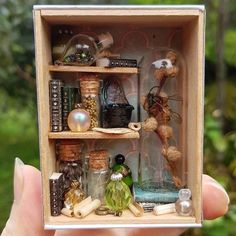 a hand holding up a miniature shelf with various items in it