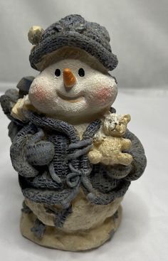 a snowman figurine holding a teddy bear and wearing a knitted hat