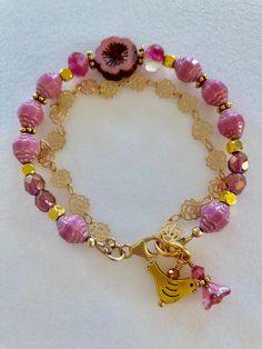 Lovely double strand beaded Premium Czech glass flower bracelet featuring Picasso pink turbine beads, Czech pink sea glass, pink cherub fire polished crystals, and single 15 mm pink Picasso pansy flower. All accented with antique gold plated daisies and shiny cubes. Satin Hamilton rose chain adds the perfect delicate second strand. Premium gold electroplated brass chain in satin finish with intricate rose flower pattern. Bracelet is beaded on professional Soft Flex beading wire with high quality Adjustable Pink Charm Bracelet With Spacer Beads, Pink Beaded Czech Glass Jewelry, Pink Flower Glass Jewelry, Pink Flower-shaped Glass Jewelry, Adjustable Pink Single Strand Beaded Bracelets, Adjustable Pink Single Strand Beaded Bracelet, Adjustable Single Strand Pink Beaded Bracelet, Pink Charm Bracelet For Jewelry Making With Spacer Beads, Adjustable Pink Glass Bracelets