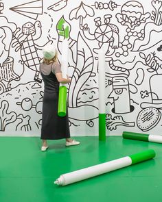 a woman standing in front of a wall with green marker markers on it and another drawing behind her