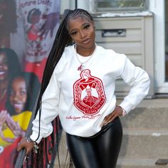 a woman with long braids wearing a white sweatshirt and black leggings standing in front of a building