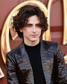 a young man with curly hair wearing a black turtle neck sweater and leather blazer