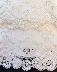 a white lace tablecloth with flowers and leaves on the edge is laying on a black surface