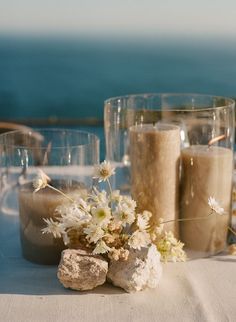 there are two glasses and some rocks on the table with flowers in front of them