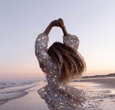 a woman standing on top of a beach next to the ocean holding her arms up