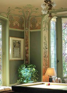 a pool table in front of two stained glass windows and a potted plant on the other side