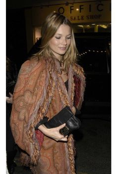 a woman is walking down the street carrying a purse and wearing a shawl over her shoulders