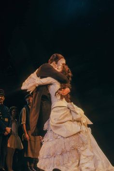 a man and woman embracing each other in the middle of a stage scene with people looking on