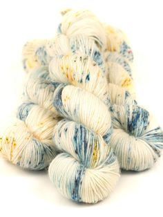 several skeins of white and blue yarn on top of each other with yellow speckles