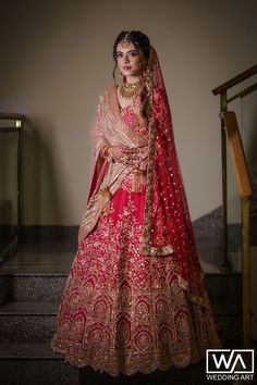 a woman in a red and gold bridal gown standing on stairs with her hands behind her head