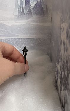 a hand is holding a small black object in the middle of a room with snow on the floor