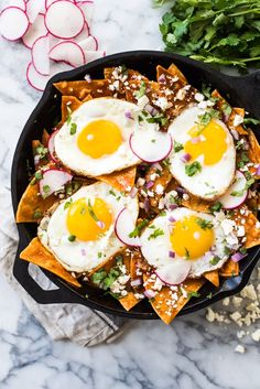 two fried eggs on top of scrambled eggs in a skillet with green onions and peppers