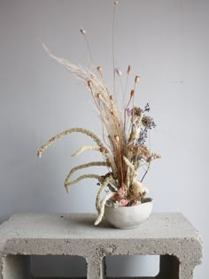 a white bowl filled with lots of flowers on top of a cement block table next to a wall