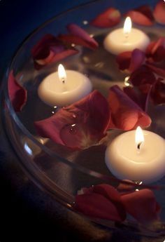 several candles are floating in a bowl with rose petals on the bottom and one candle is lit