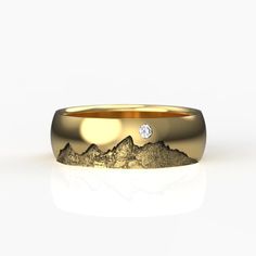 a yellow gold wedding band with a diamond in the center and mountains on it, against a white background