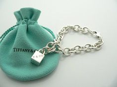 Offered for sale is a wonderful and super cute Tiffany and Co. Sterling Silver 1837 Cube / Box Charm bracelet.   The piece is made from substantial and bright Tiffany silver, and yet retains a very feminine feel to it.  Attached to its very substantial and bright Tiffany Silver charm bracelet is a super Cool 1837 Cube Padlock charm.  The Gift Box padlock charm is permanently attached to the bracelet - so you will not ever have the risk of losing the charm!  It is a classic Tiffany piece that Tiffany And Co Bracelet, Tiffany T, Gold Rings Fashion, Silver Charm Bracelet, Tiffany And Co, Gift Pouch, Bracelet Bangle, Stunning Jewellery, Pendant Bracelet