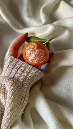 someone is holding an orange on top of a white blanket with their hands in the air