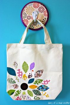 a white tote bag hanging on a blue wall next to a plate with a flower design