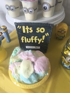 a table topped with a cake covered in frosting next to minion cupcakes