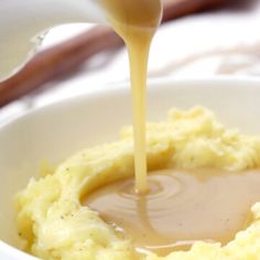 a spoon pouring gravy over mashed potatoes in a white bowl