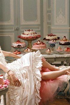 a woman in a dress sitting on a chair next to a table filled with cakes and cupcakes