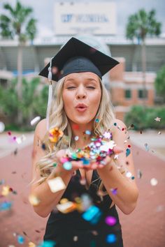 a woman wearing a graduation cap and gown blowing confetti in front of her