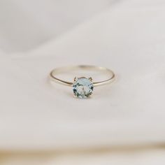 a white gold ring with an aqua blue topazte in the center on a white cloth