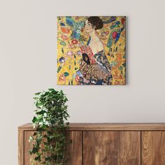 a painting hanging on the wall above a wooden cabinet with a potted plant in front of it