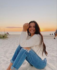 a woman sitting in the sand with her hand on her head and smiling at the camera