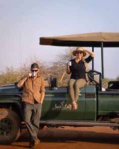 a man and woman sitting on the back of a green truck in front of a safari vehicle