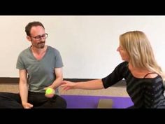 a man and woman sitting on the floor with a tennis ball