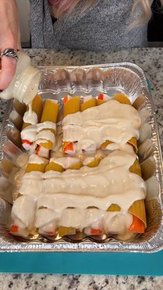 a woman is pouring dressing on some food in a baking dish with carrots and celery