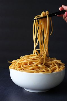 a person is eating noodles with chopsticks in a white bowl on a black surface