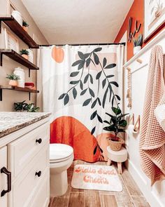 a bathroom with orange and white decor on the shower curtain, toilet seat cover and rug