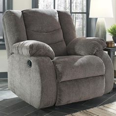 a living room with a gray recliner in front of a window and potted plant