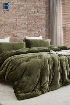 a bed with green comforter and pillows in front of a brick wall next to a window