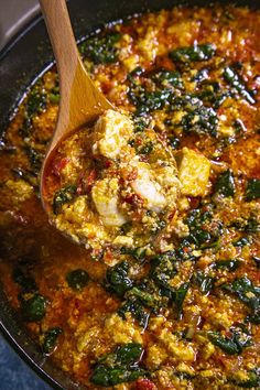 a wooden spoon is stirring some food in a large pot with red sauce and spinach