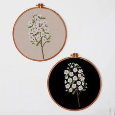 two embroidery hoops with flowers and leaves on them hanging from the side of a wall