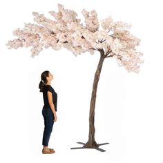 a woman standing in front of a tree with white flowers on it's trunk