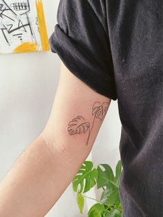 a person with a tattoo on their arm and palm trees behind them, in front of a potted plant