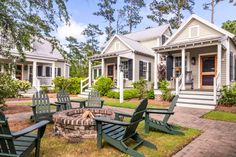 a fire pit surrounded by lawn chairs in front of two white houses with porches