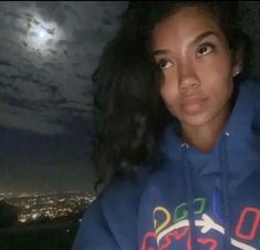 a woman wearing a blue hoodie with the moon in the sky above her head