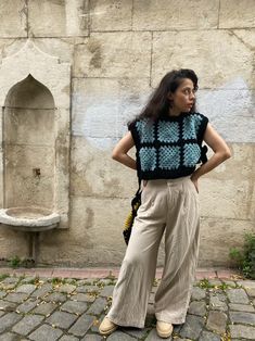 a woman standing in front of a stone wall with her hands on her hips and looking off to the side