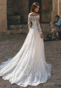 a woman in a white wedding dress standing on a cobblestone street with her back to the camera