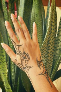 a person's hand with a tattoo on it next to some plants and a potted plant